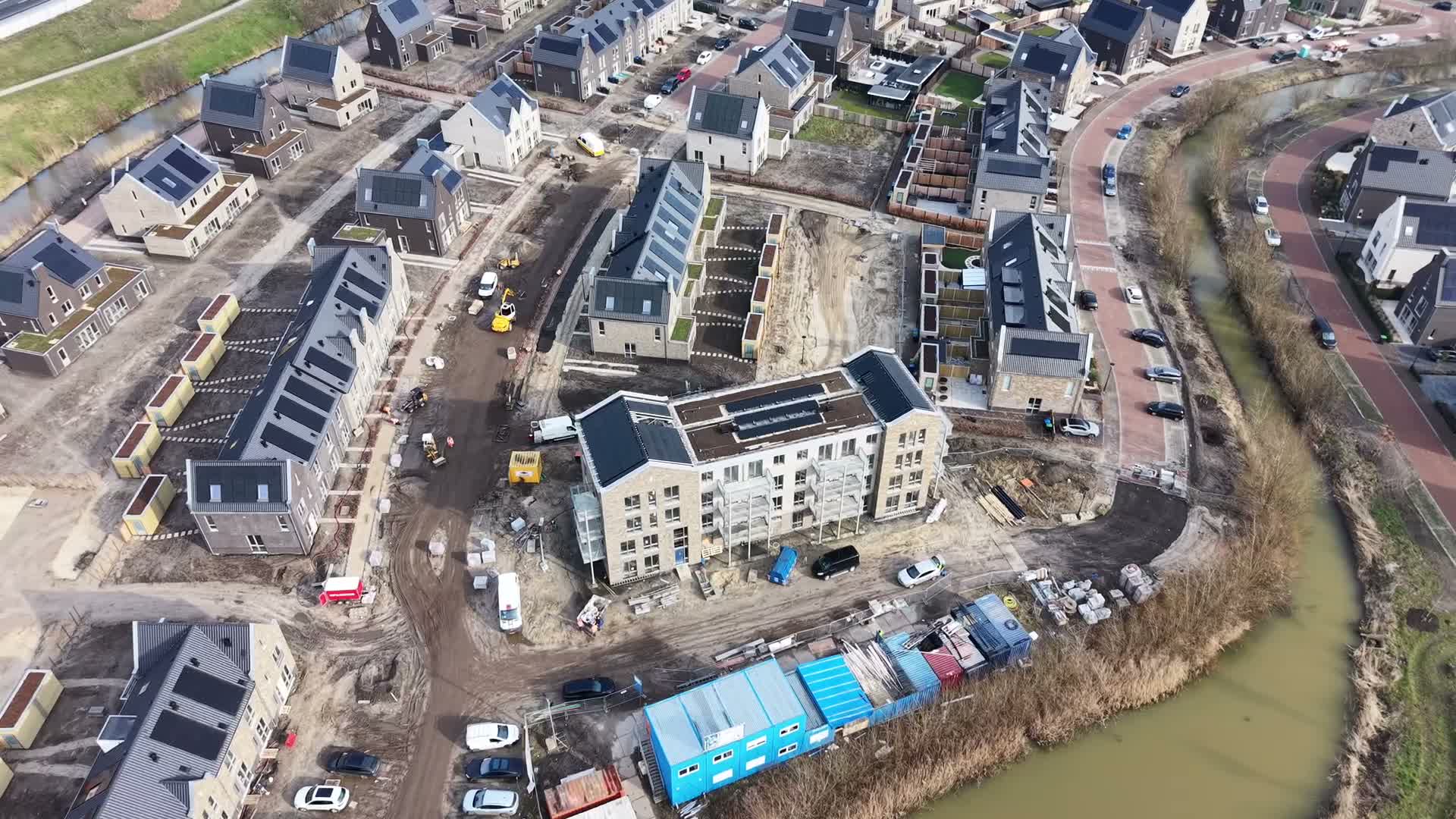 Luchtfoto van een nieuwbouwwijk met zonnepanelen op de daken, naast een watergang